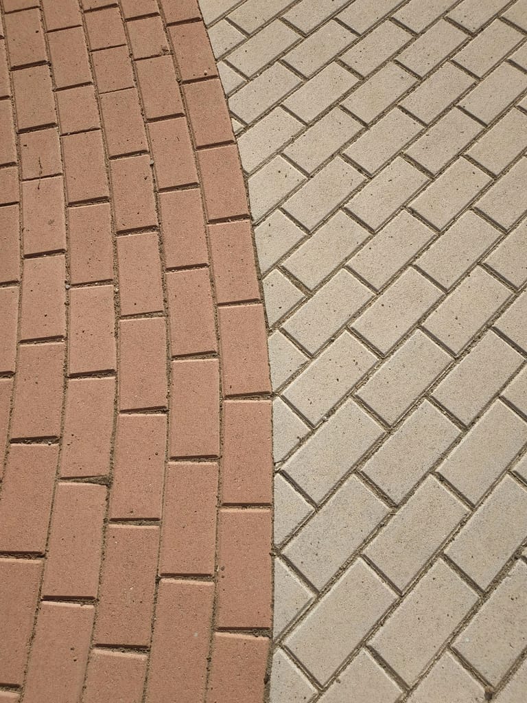 Curved red-brick path meeting cream herringbone paving