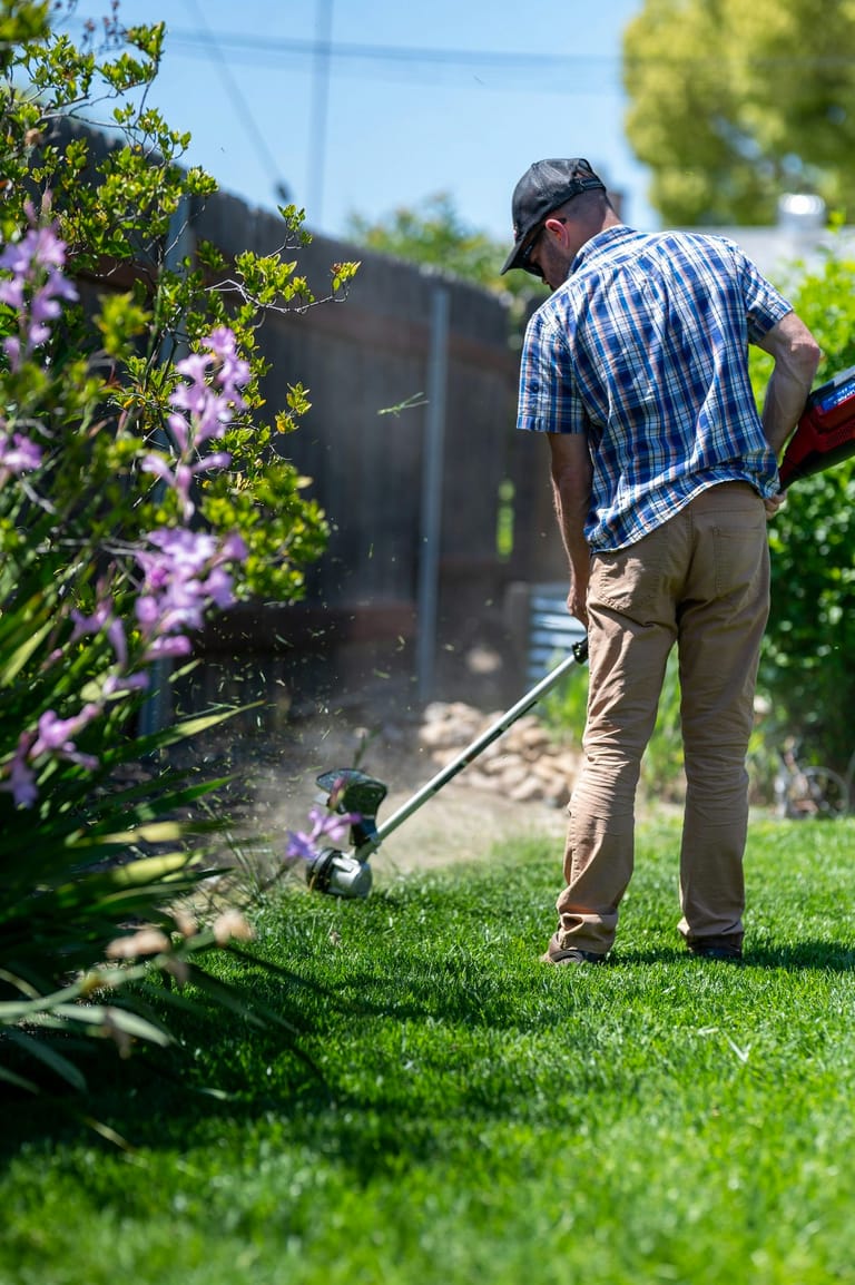 Gardener line-trimming a lawn edge on a maintenance visit