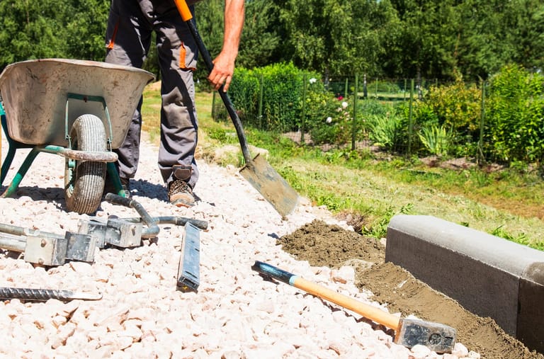 Landscaper spreading soil beside a new white-pebble path and concrete edging